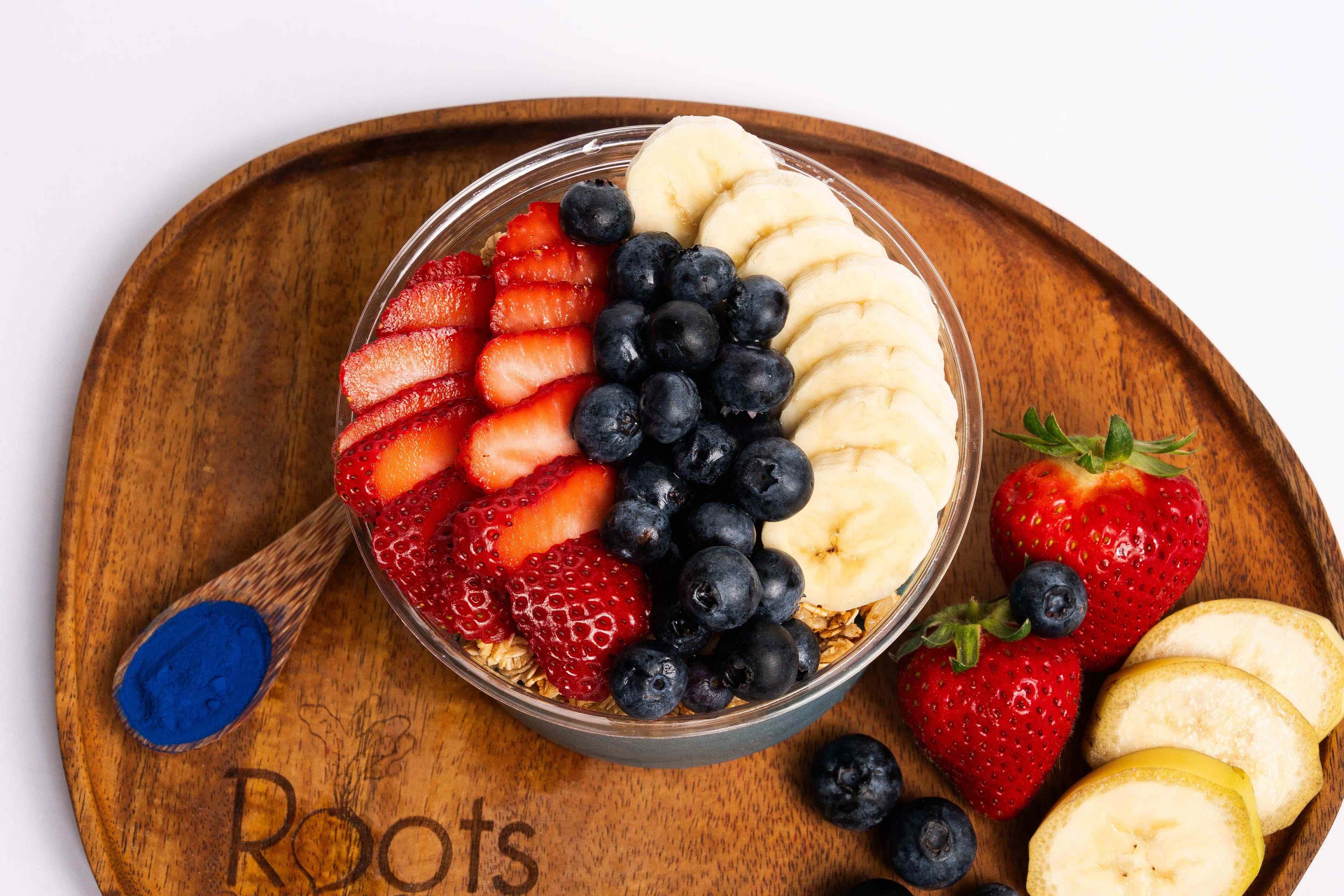 Açaí bowl topped with strawberries, blueberries, and banana on a wooden board